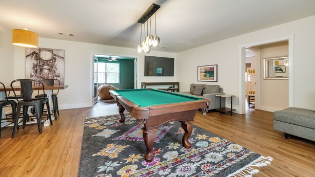 A living room with a pool table, a dining area with chairs, a sofa, and a rug.