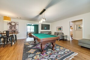 Una sala de estar con mesa de billar, comedor con sillas, sofá y alfombra.