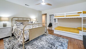 A bedroom with a single bed, a bunk bed, a ceiling fan, a bedside table with a lamp, and a patterned rug.