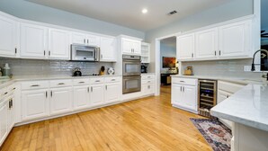 A modern kitchen with white cabinetry, stainless steel appliances, and a wooden floor.