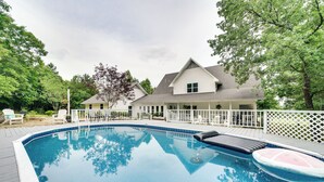 A swimming pool with a deck, surrounded by a white fence and trees.
