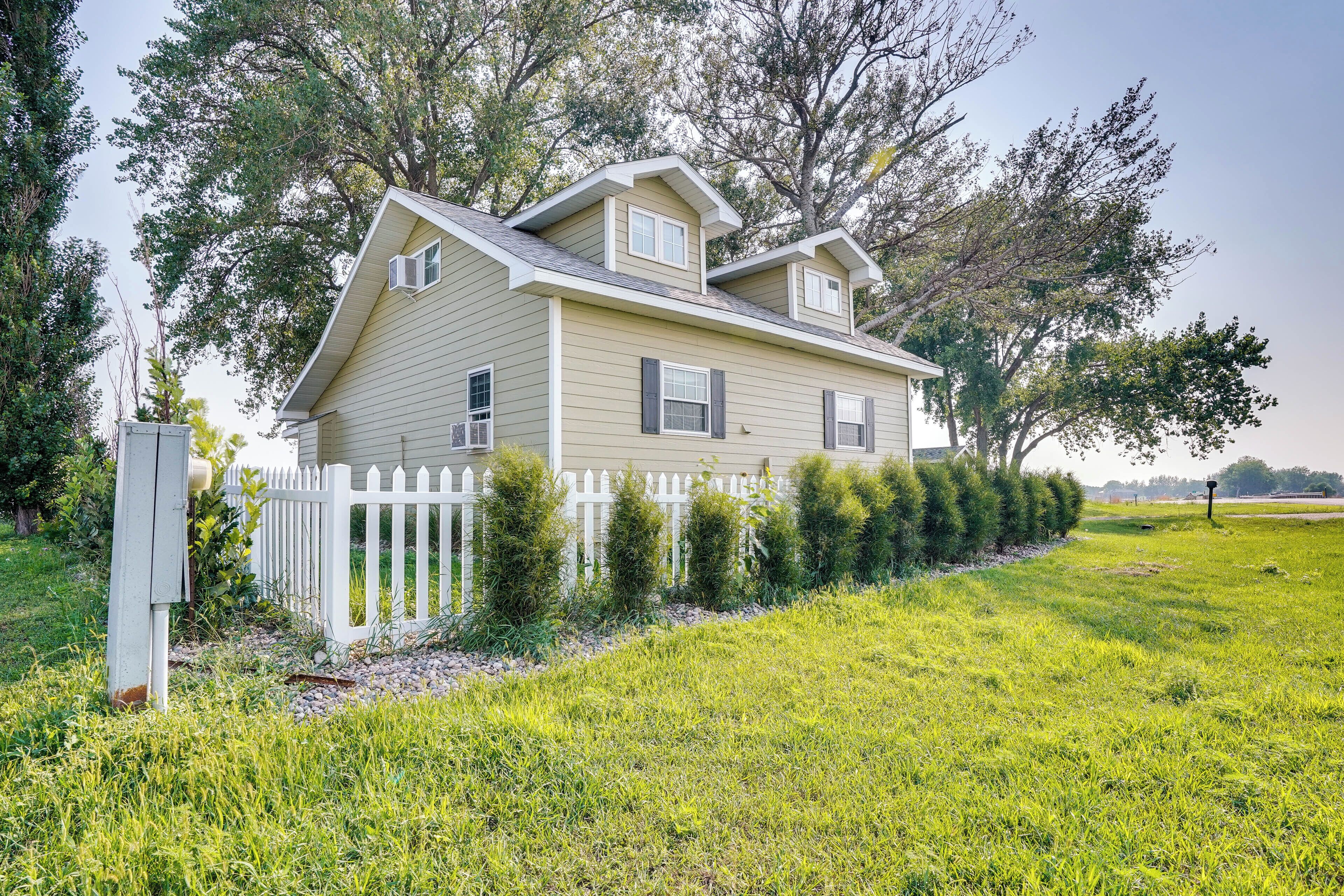 A two-story house with a white picket fence, surrounded by well-maintained grass and trees.