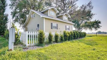 A two-story house with a white picket fence, surrounded by well-maintained grass and trees.