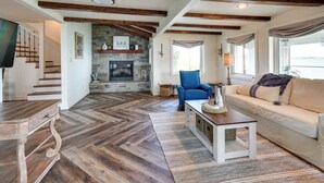 A spacious living room with a stone fireplace, wooden beams, a sofa, and a television. - Waterfront Lake Poinsett Retreat w/ Fire Pit! (Castlewood)