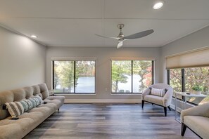A spacious living room with a large window, a ceiling fan, and a sofa with a patterned throw pillow. - Spacious Lake Norman Retreat w/ Boat Ramp! (Sherrills Ford)