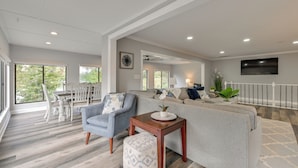 A spacious living room with a grey sofa, a blue armchair, and a wooden side table. There is a dining area with white chairs and a table in the background. - Spacious Lake Norman Retreat w/ Boat Ramp! (Sherrills Ford)