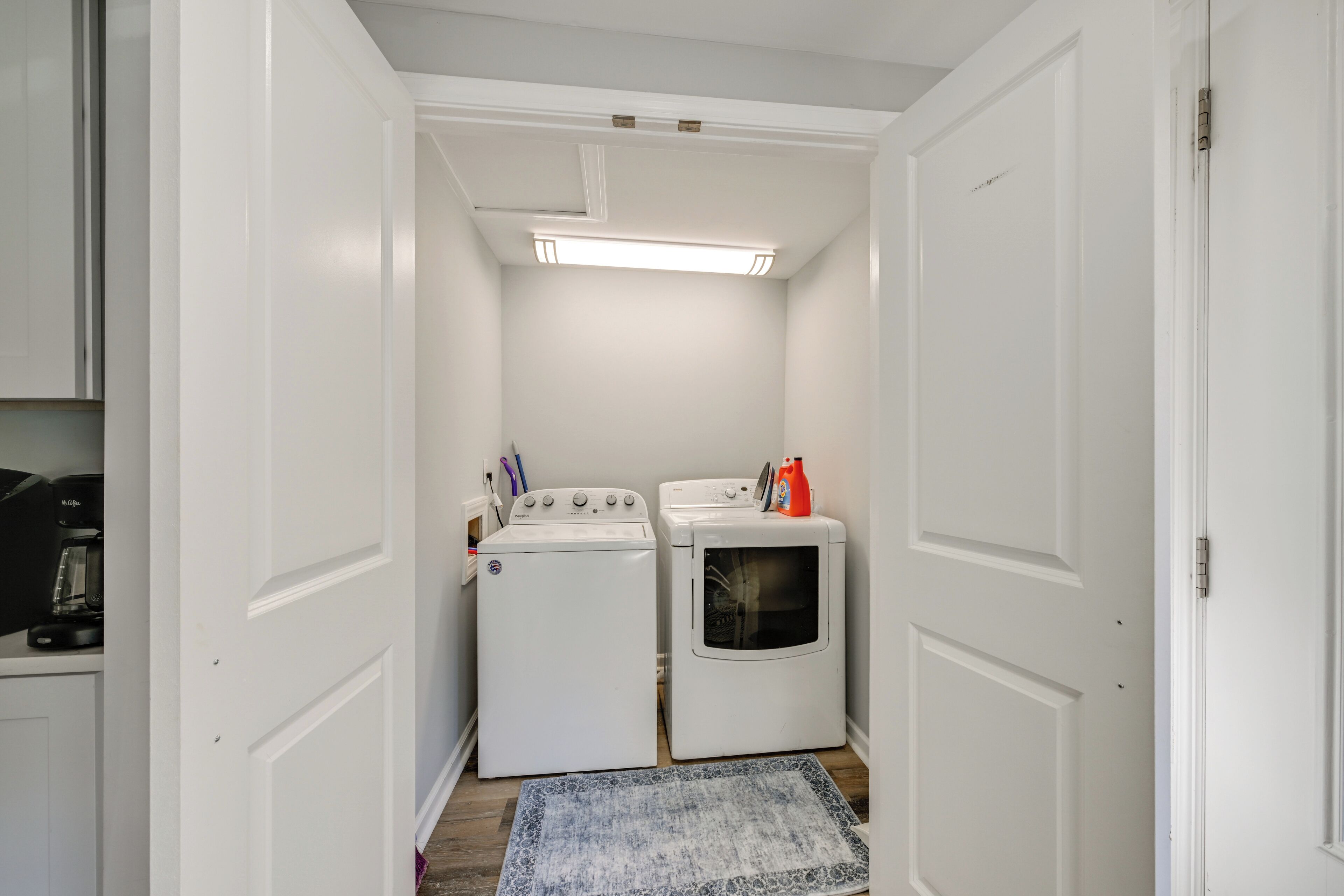 A laundry room with two washing machines and a dryer, a coffee maker, and a red bottle on the dryer.