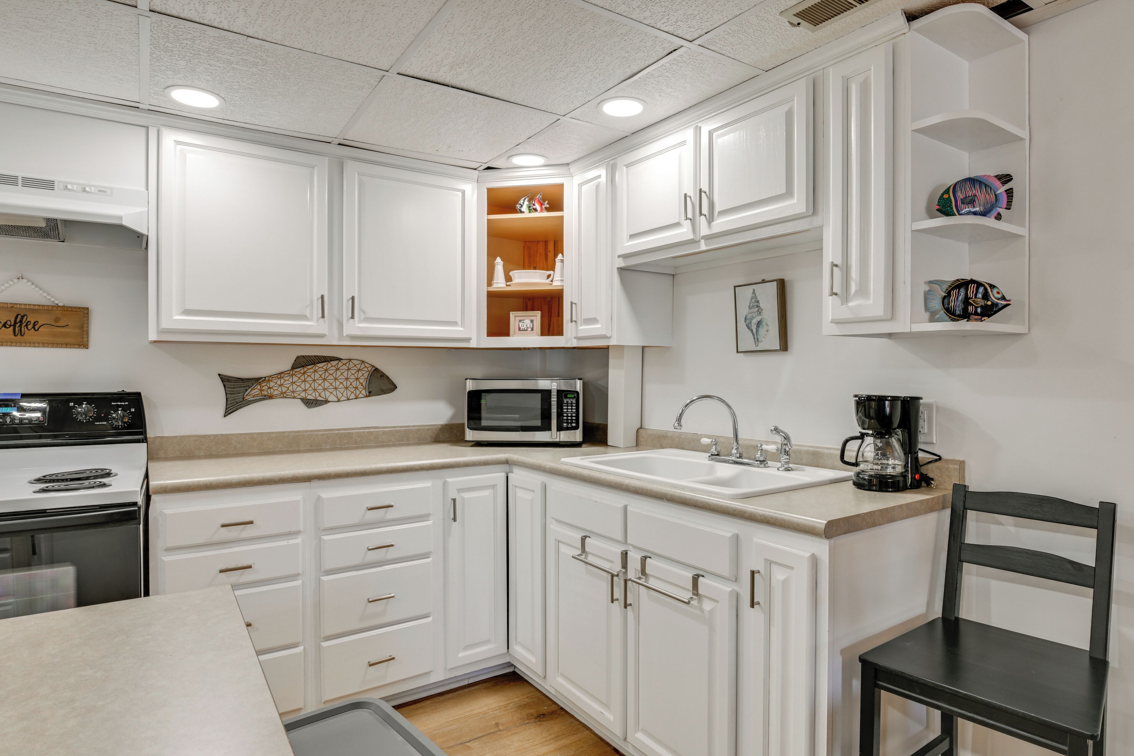 A modern kitchen with white cabinets, a microwave, a coffee maker, and a sink.