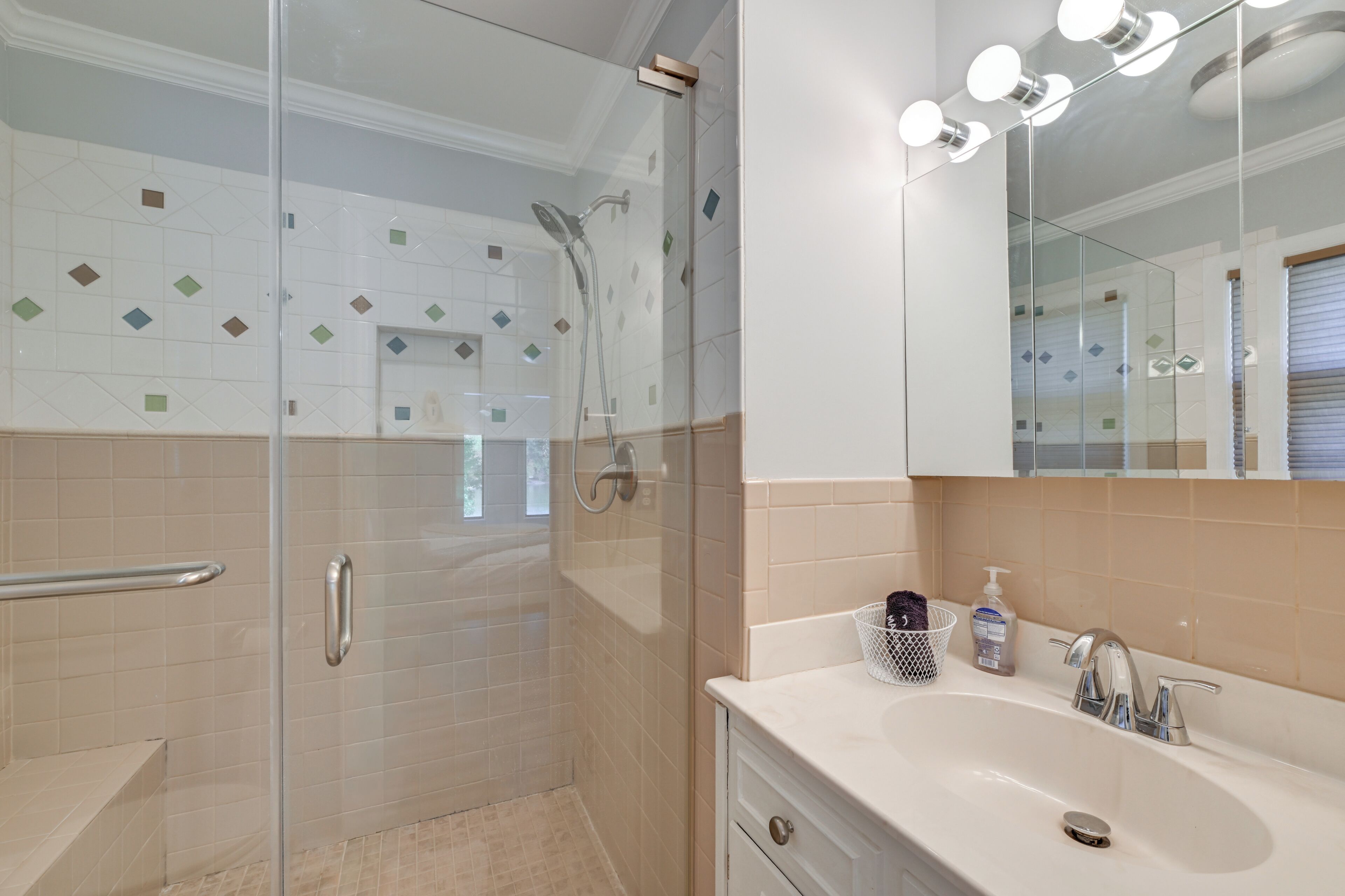 A modern bathroom with a glass-enclosed shower, a white sink with a mirror, and a beige tiled wall.