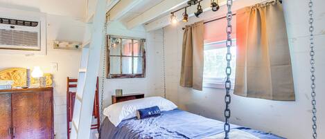 Un dormitorio con cama, armario de madera, espejo y ventana con cortinas.