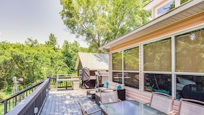 Una terraza con mobiliario exterior, una parrilla cubierta y grandes ventanas con vistas a un área boscosa.