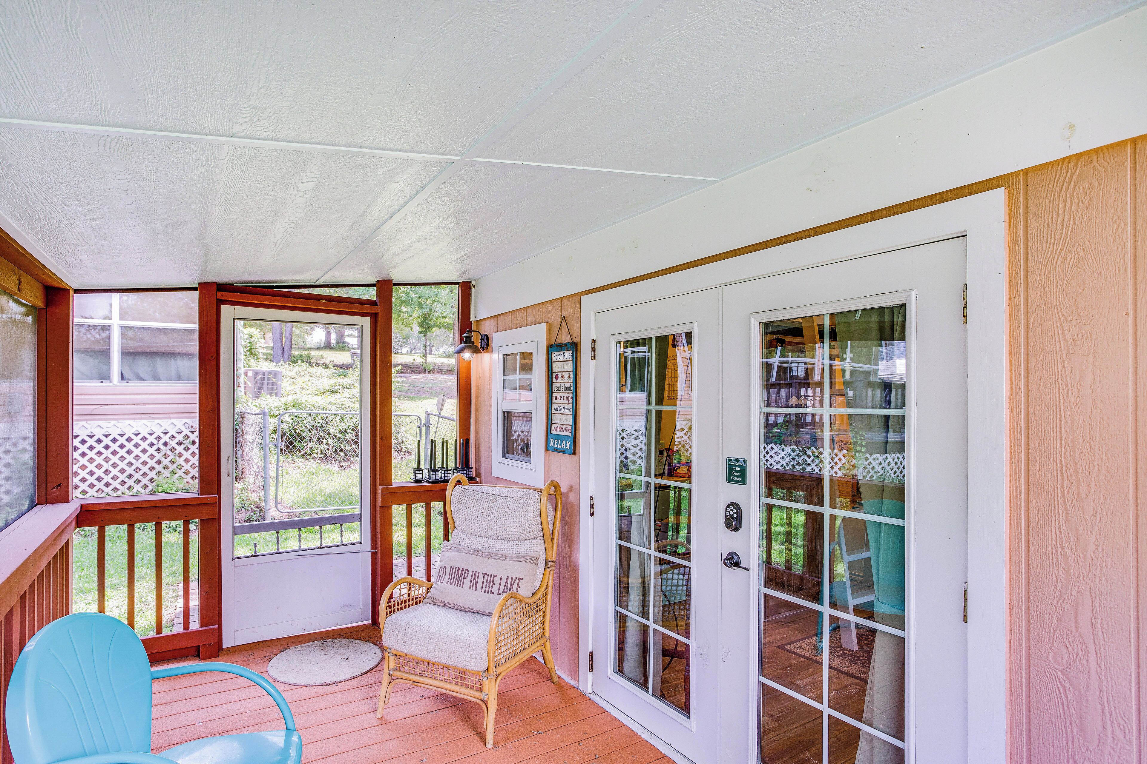 A covered porch with a wicker chair, a blue chair, and a glass door leading to a patio area.