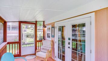 A covered porch with a wicker chair, a blue chair, and a glass door leading to a patio area.