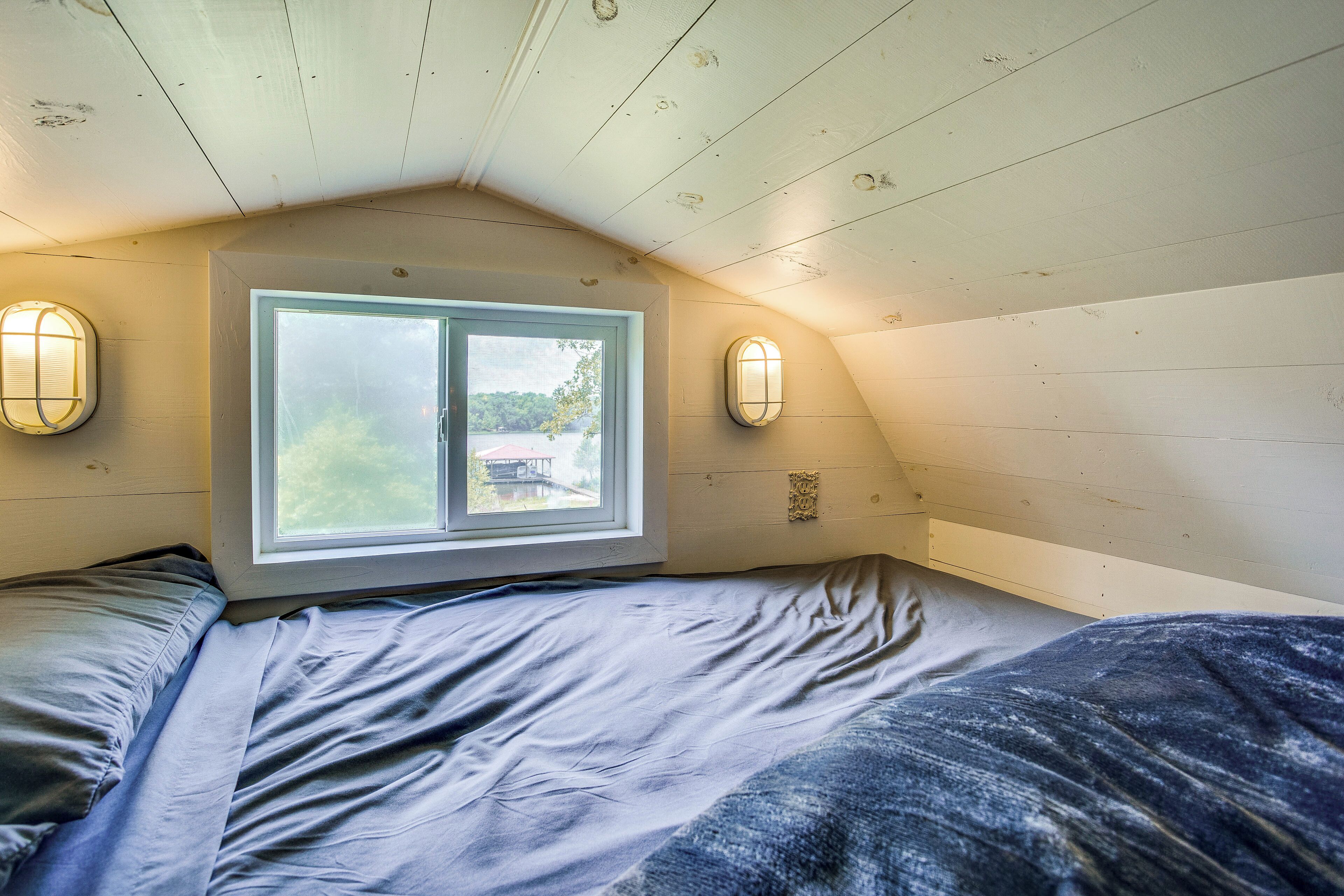 A bedroom with a sloped ceiling, a large window, and two wall-mounted lights.