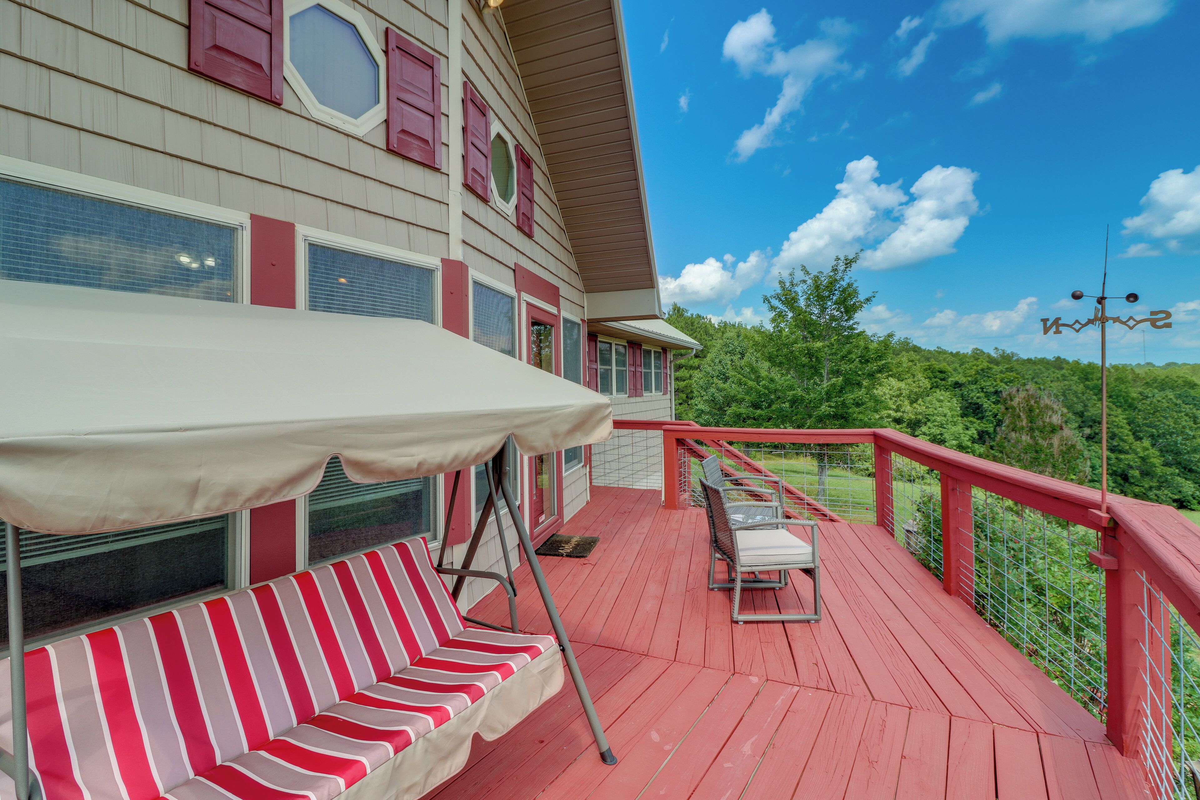 A red deck with a white canopy, striped red and white lounge chairs, and a metal railing.