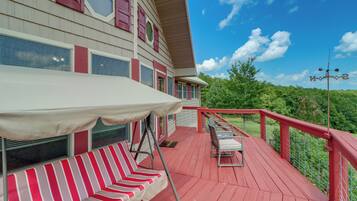 A red deck with a white canopy, striped red and white lounge chairs, and a metal railing.
