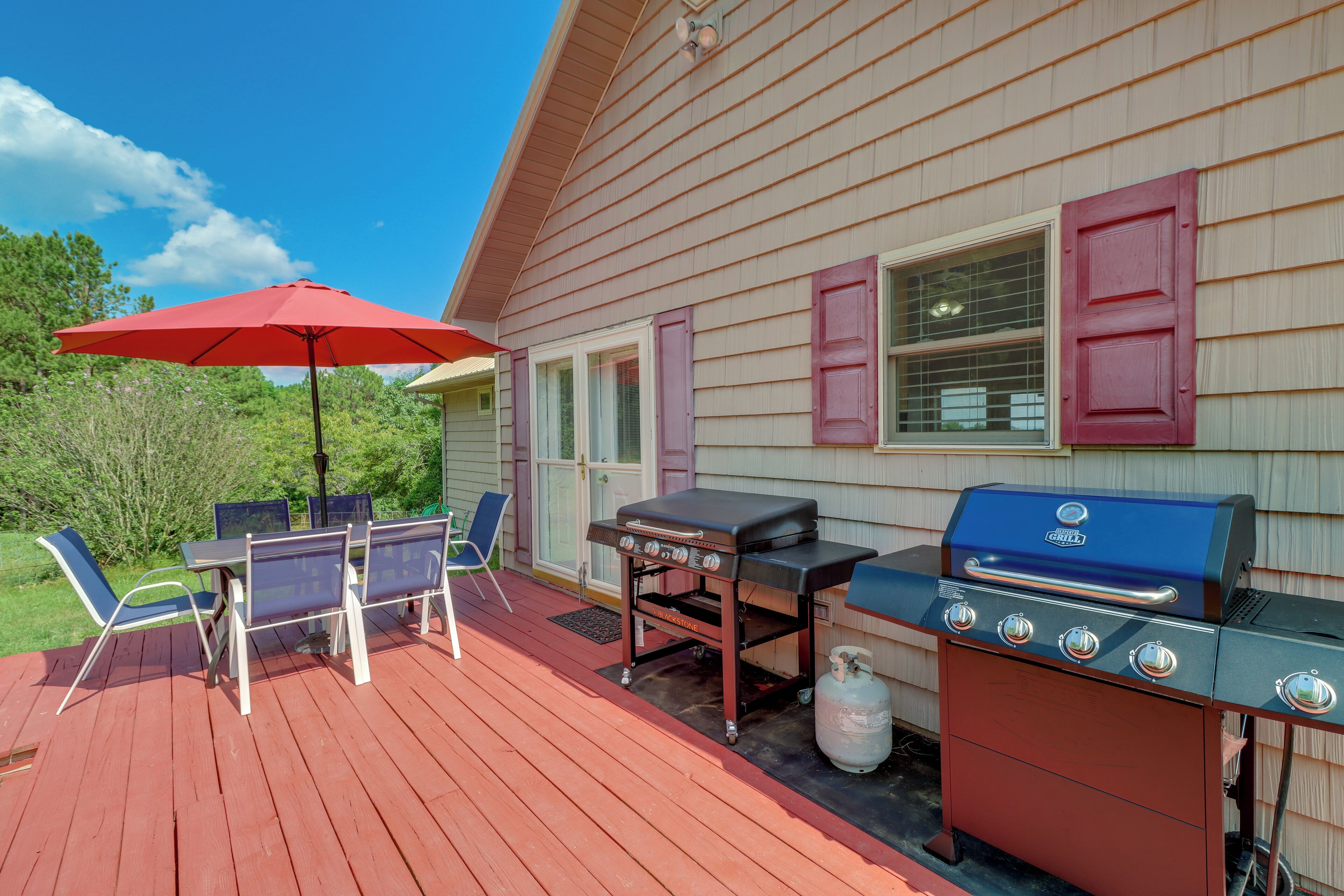 A deck with a grill, chairs, and an umbrella.