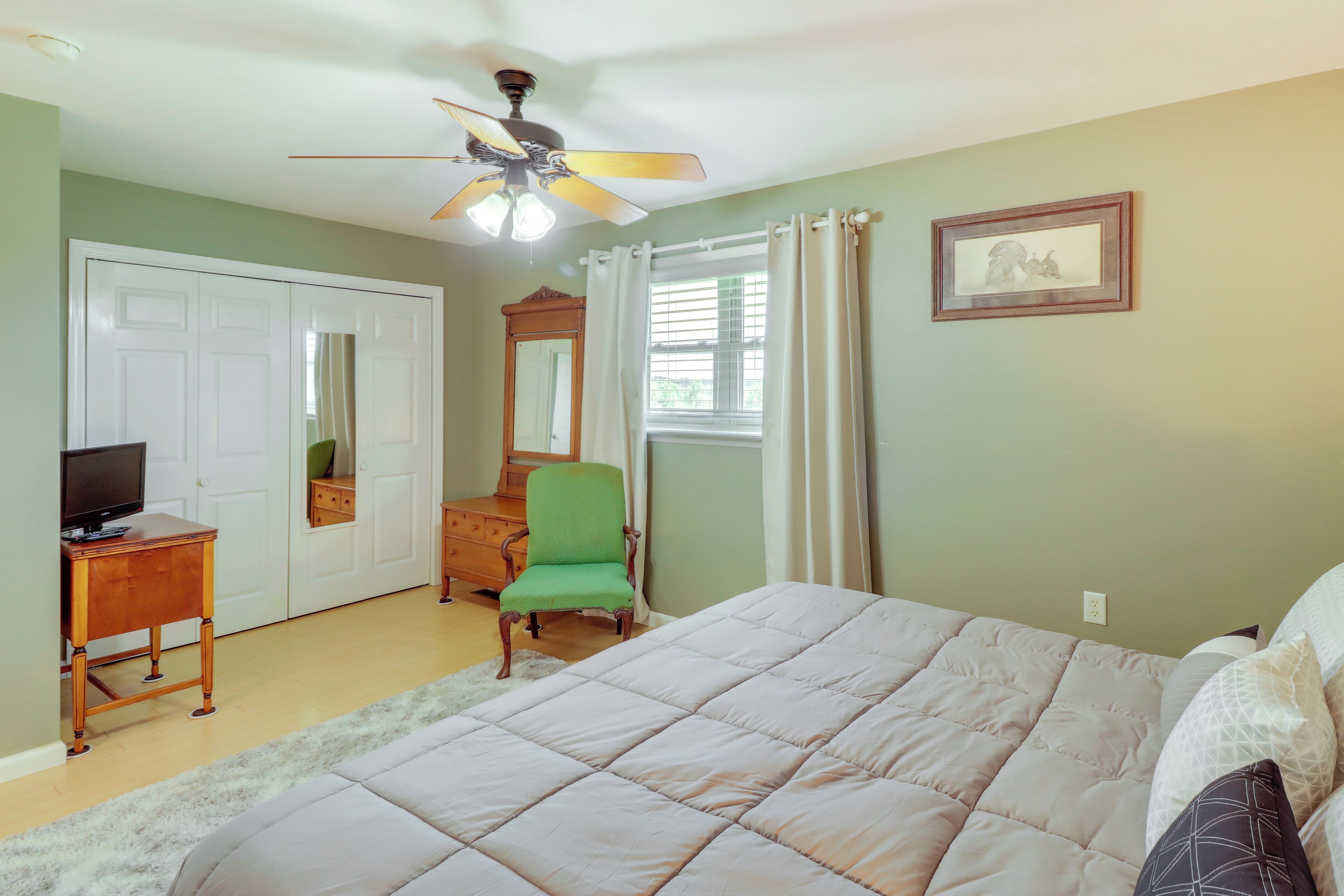 A bedroom with a bed, a desk, a chair, a ceiling fan, and a window with curtains.