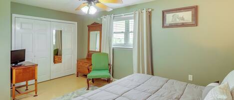 A bedroom with a bed, a desk, a chair, a ceiling fan, and a window with curtains.