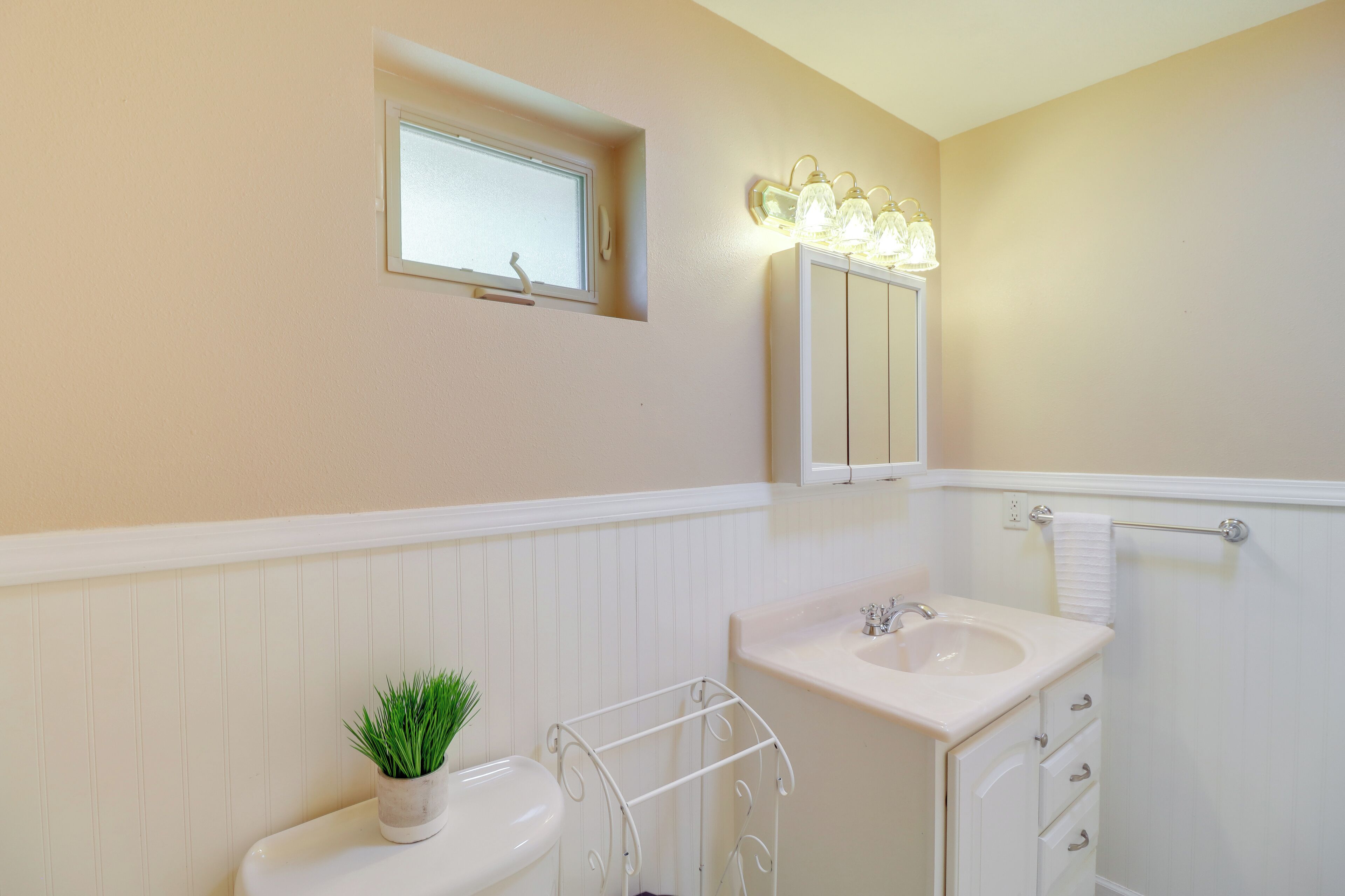 A bathroom with a toilet, sink, and mirror. There is a small window above the toilet and a towel rack next to the sink.