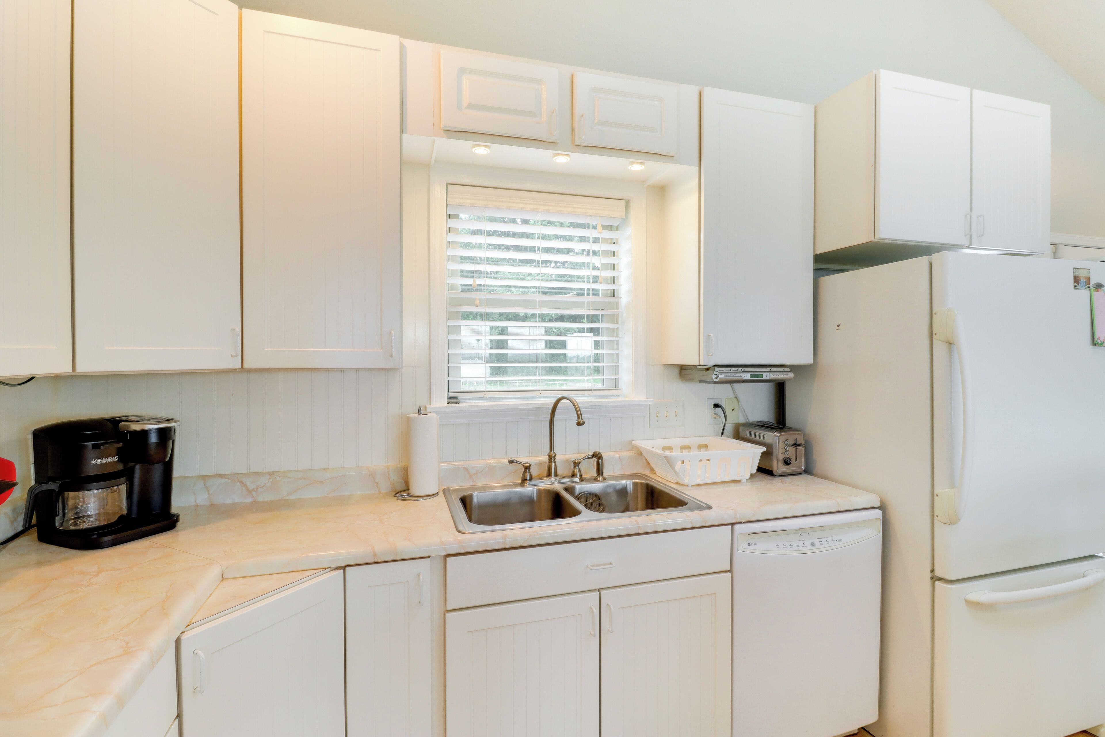 A kitchen with white cabinets, a double sink, a coffee maker, a toaster, and a refrigerator.