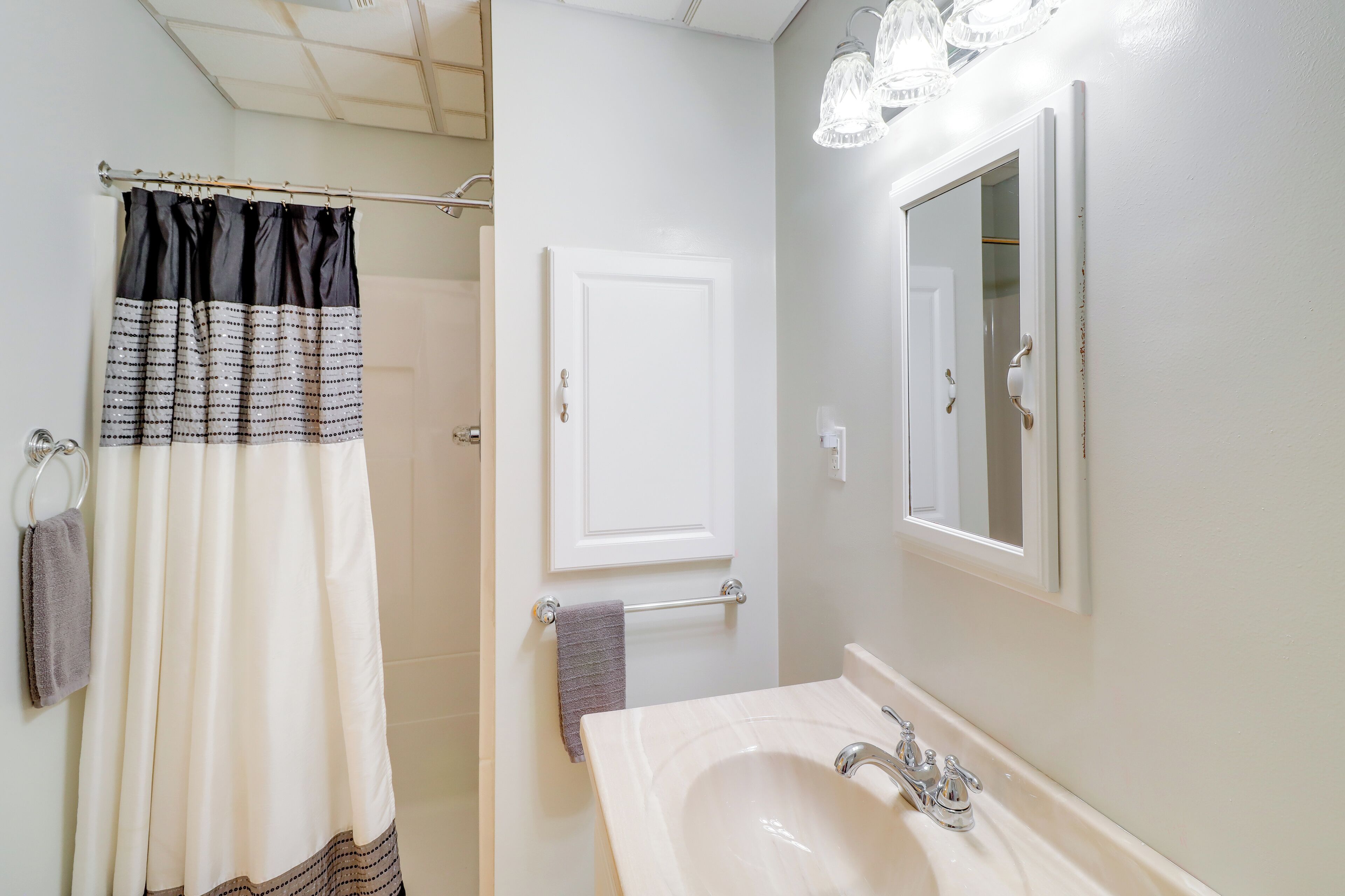 Une salle de bain avec un rideau de douche, un porte-serviettes, un lavabo avec un miroir et une porte.