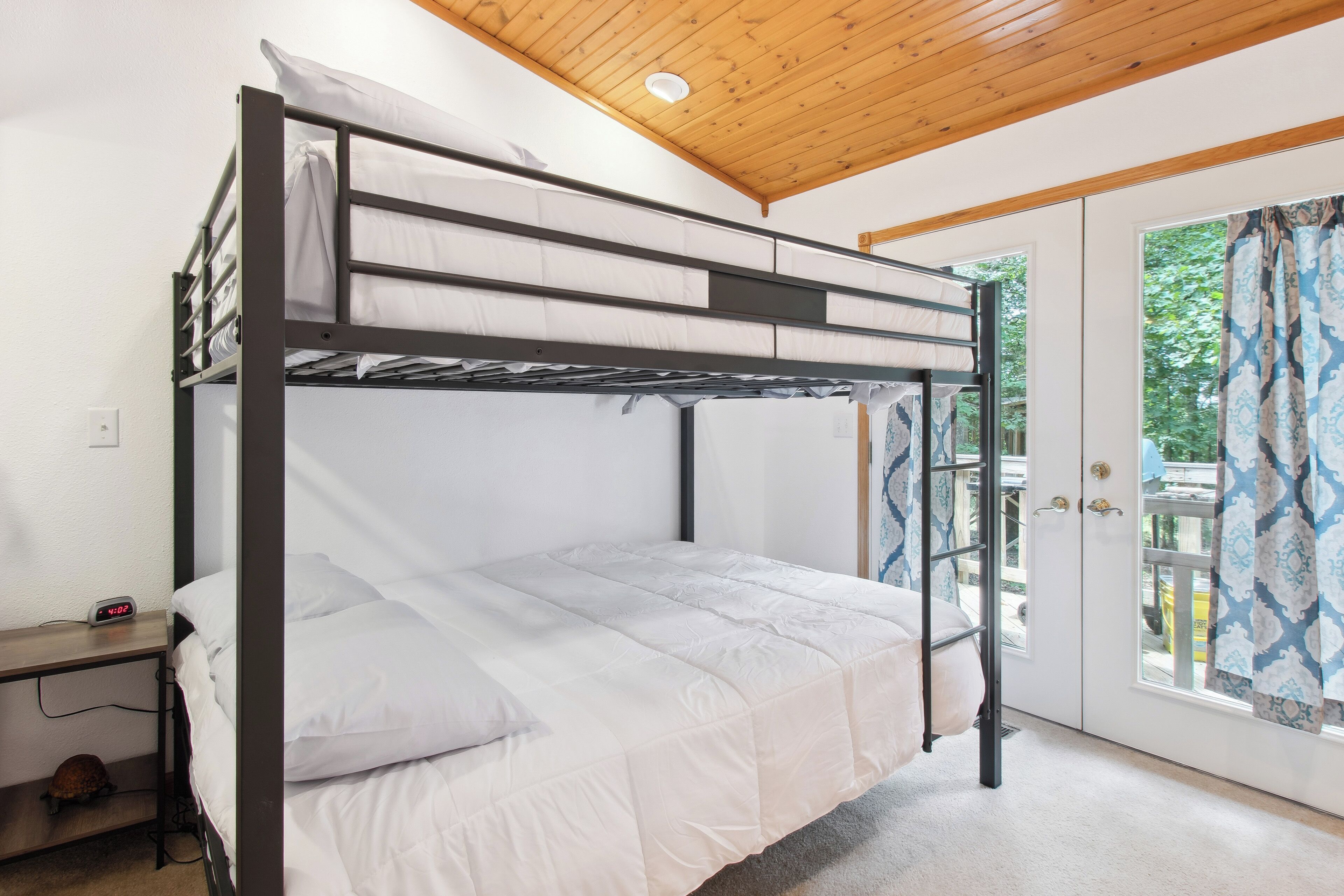 A bunk bed room with a desk, a clock, and a view of the outside.