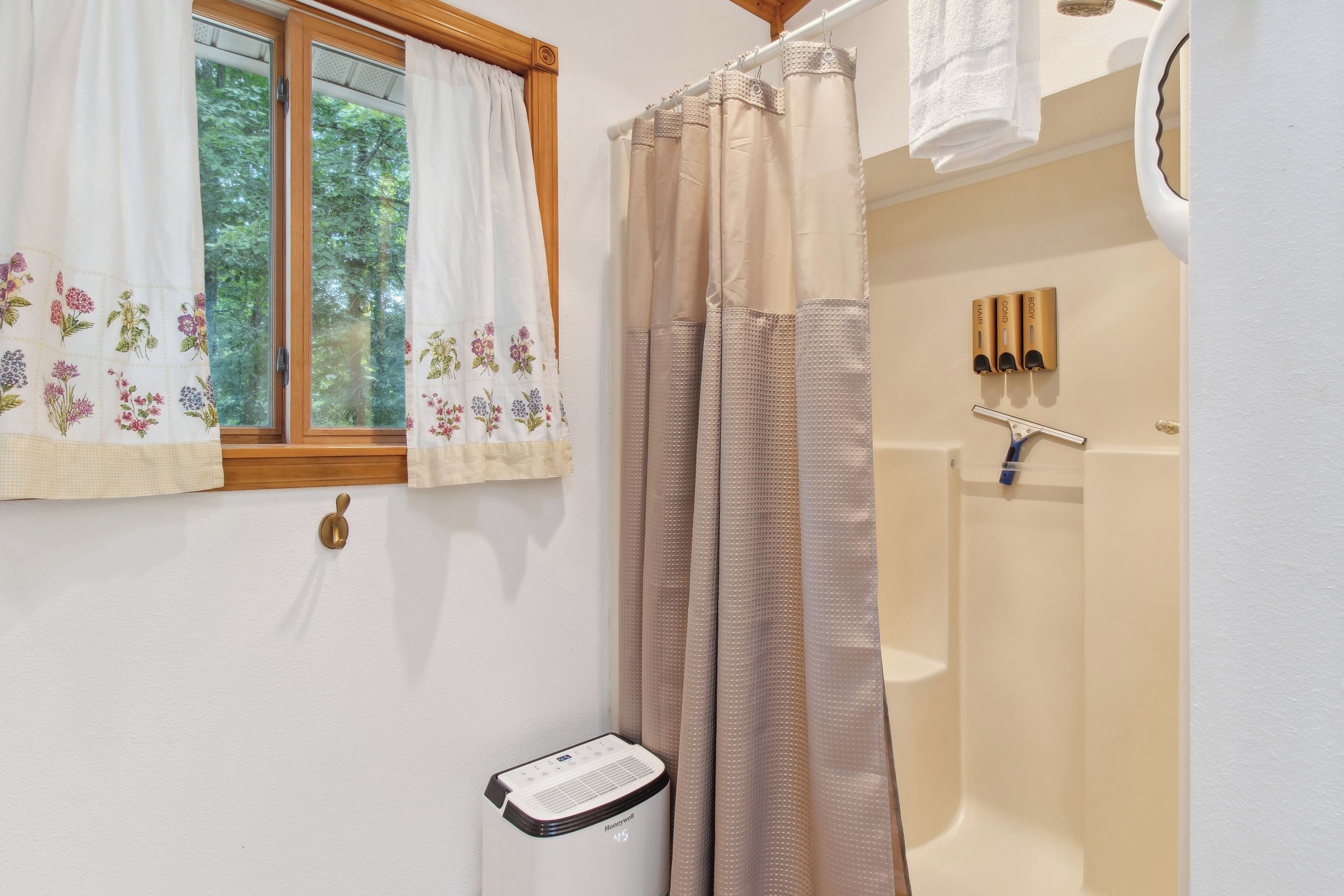 Un baño con ducha, una ventana con cortinas florales y un perchero para toallas.
