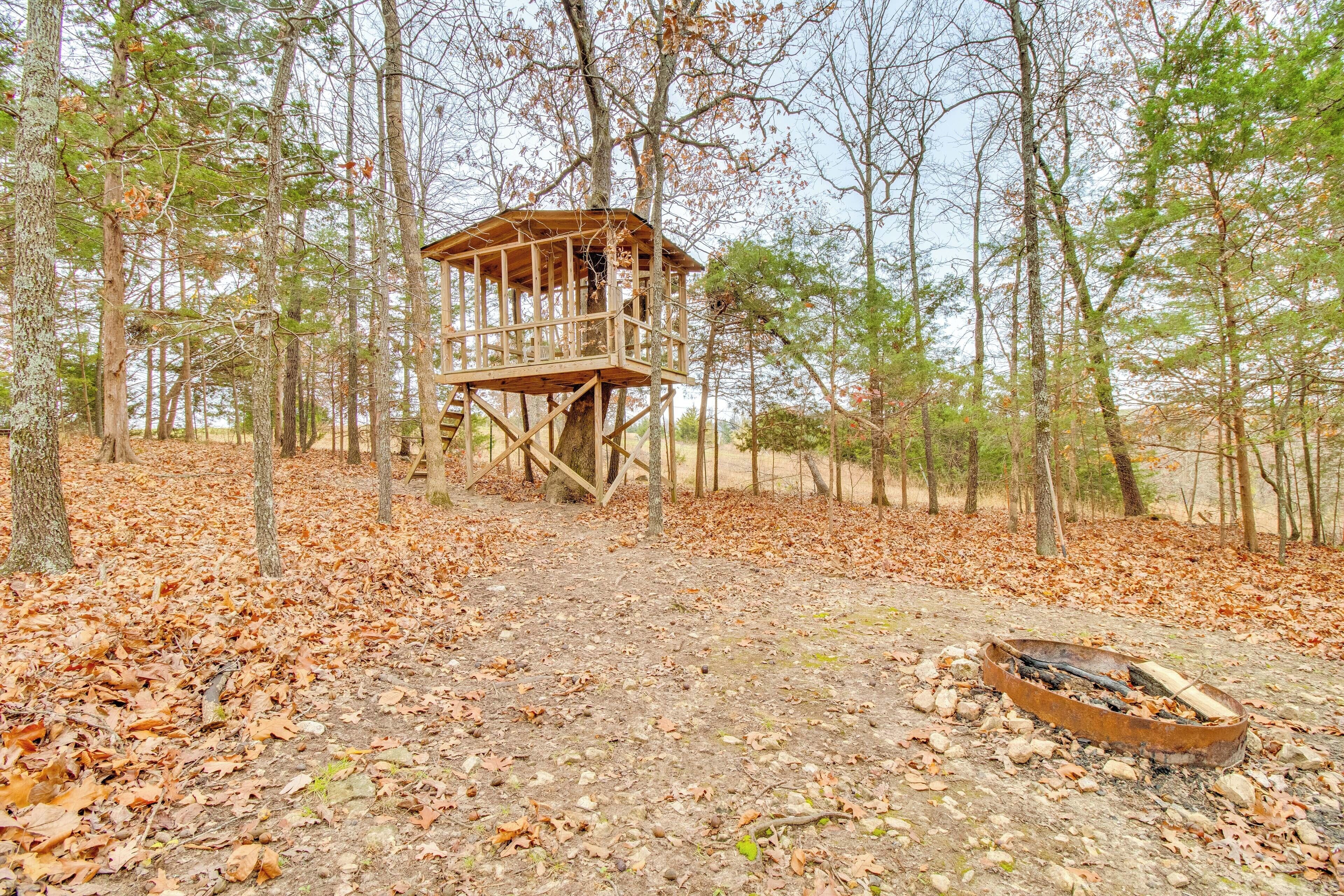 A wooden lookout tower in a forest with a fire pit nearby.