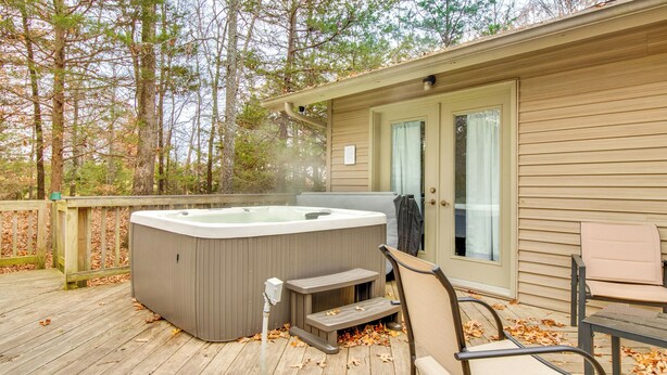 A hot tub on a wooden deck with a chair and a table, surrounded by trees. - Serene Yellville Retreat w/ Hot Tub on 85 Acres (Yellville)