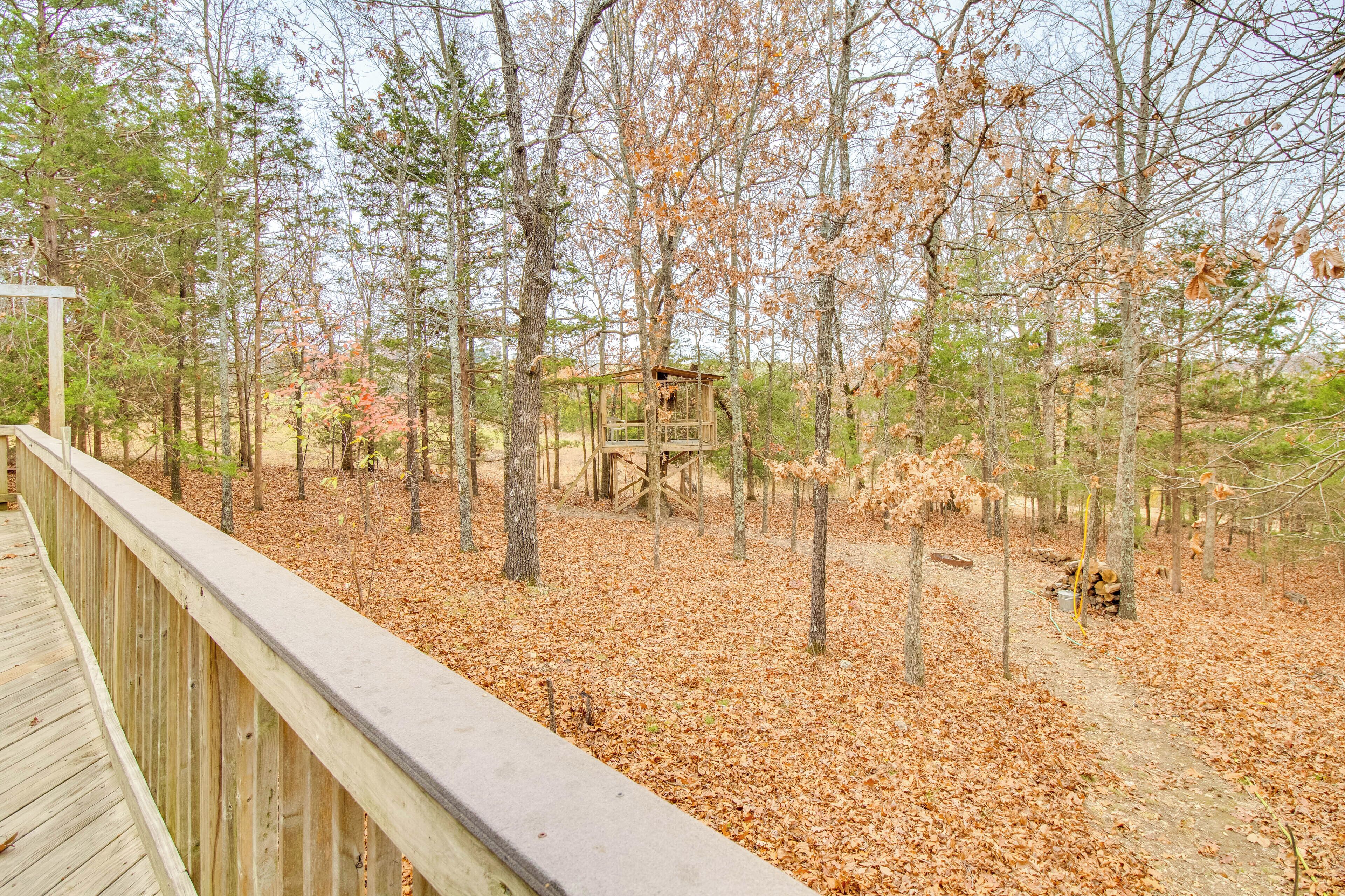 A wooden deck overlooking a forested area with a wooden structure in the distance.