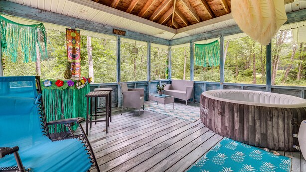 A covered outdoor deck with wooden flooring, a hot tub, wicker furniture, and a hanging chair.
