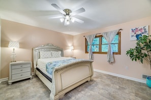 A bedroom with a bed, nightstand, lamp, ceiling fan, window with curtains, and a potted plant. - Peaceful Pocono Retreat: Hot Tub & Covered Deck! (Stroudsburg)