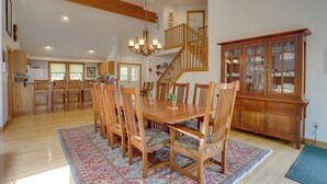 Une salle à manger spacieuse avec une table et des chaises en bois, un lustre et un escalier menant à un niveau supérieur.