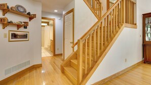 Un escalier en bois avec une rampe, une porte blanche et un couloir au plancher en bois.
