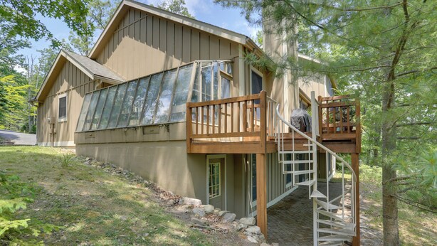 Une maison à deux étages dotée d’une terrasse en bois et d’un escalier menant à un balcon situé au deuxième étage.