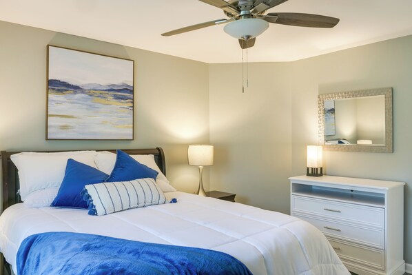 A bedroom with a bed, a ceiling fan, a nightstand with a lamp, a dresser, and a painting on the wall. - Tullahoma Vacation Rental < 8 Mi to Lynchburg! (Tullahoma)