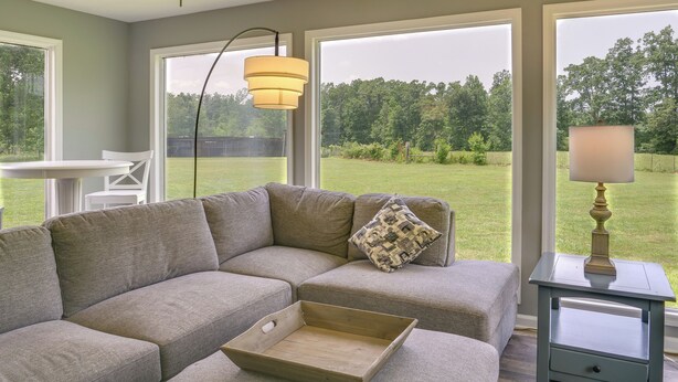 Ein modulares Sofa mit Kissen, ein Holztablett, eine Lampe und Blick auf einen grünen Garten durch große Fenster.