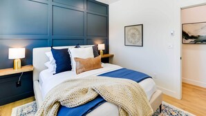 Ein modernes Schlafzimmer mit einem großen Bett, Nachttischlampen, einer dekorativen Wandverkleidung und Kunstwerken.