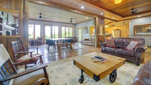 A spacious living area with a wooden ceiling, a sofa, a coffee table, and a dining table with chairs.