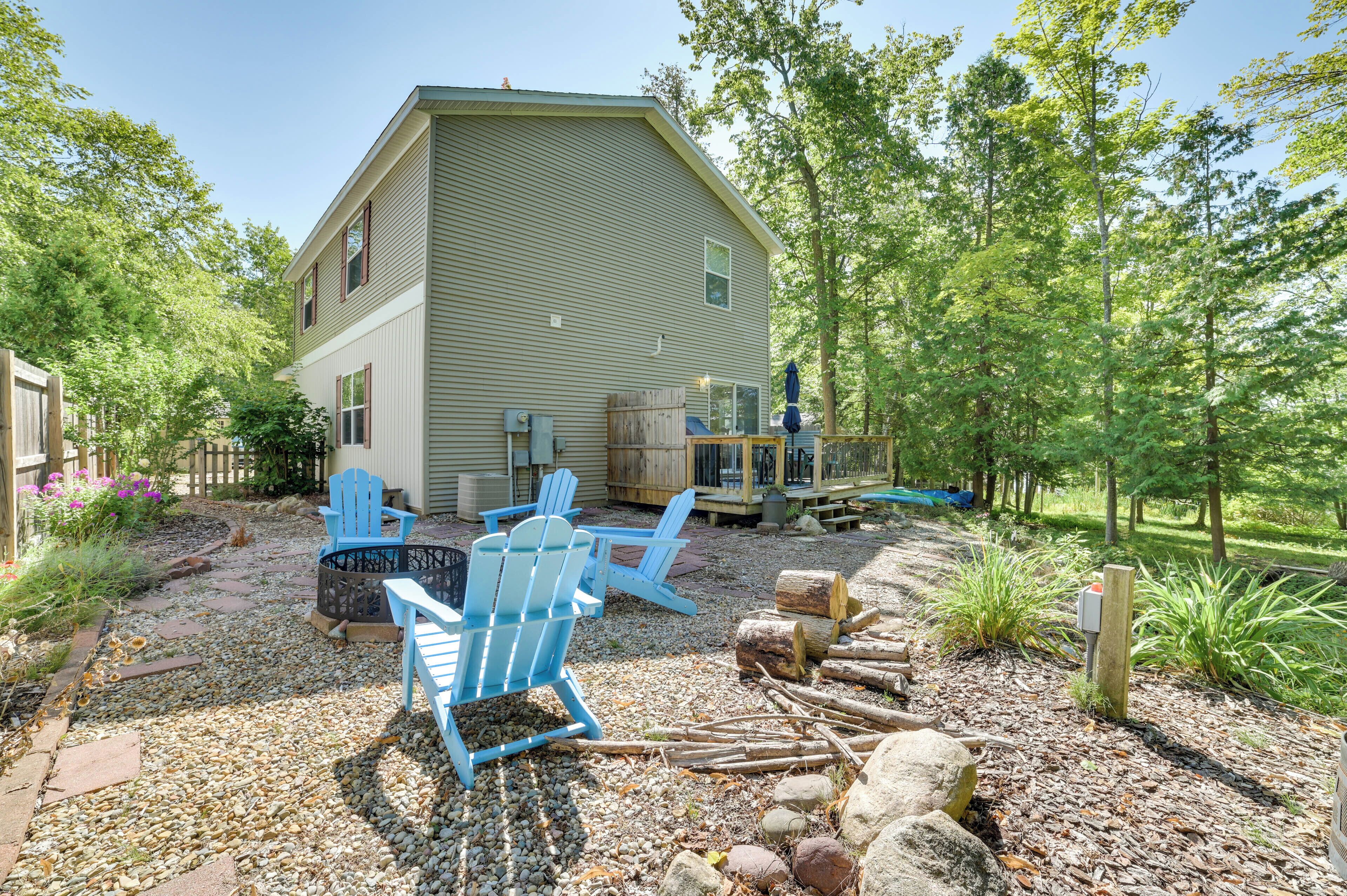 Una casa con una terraza grande, sillas Adirondack azules y un brasero.