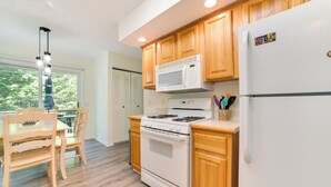 A modern kitchen with wooden cabinets, a white stove, and a refrigerator. - Walloon Lake Getaway w/ Fire Pit - Walk to Water! (Walloon Lake)