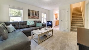 A living room with a sectional sofa, a coffee table, and a painting on the wall. - Walloon Lake Getaway w/ Fire Pit - Walk to Water! (Walloon Lake)