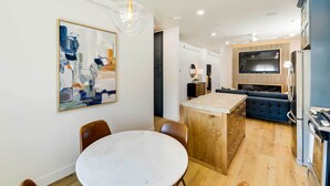 A modern kitchen with a built-in island, a dining area with a round table, and a living space with a sofa and TV. - The Lofts on 89 Condo Near Bridger Nat'l Forest! (Afton)