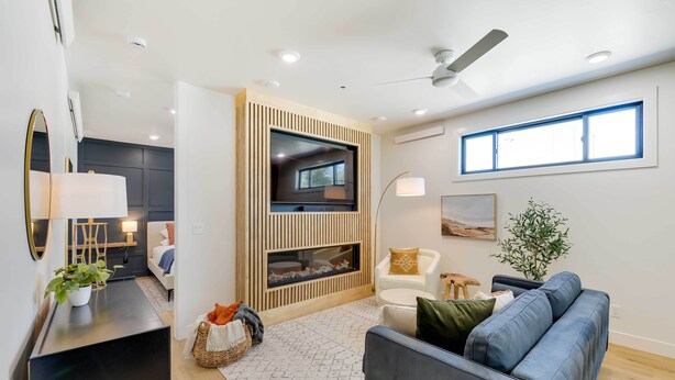 A modern living room with a flat-screen TV, a ceiling fan, and a large window. - The Lofts on 89 Condo Near Bridger Nat'l Forest! (Afton)