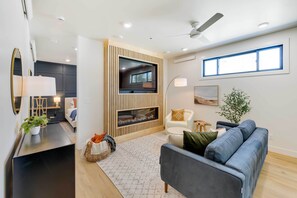 Un salon moderne doté d’un téléviseur à écran plat, d’un ventilateur de plafond et d’une grande fenêtre.