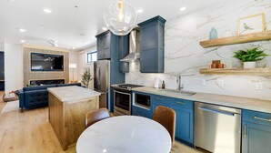 A modern kitchen with a central island, built-in appliances, and a dining area with a marble table. - The Lofts on 89 Condo Near Bridger Nat'l Forest! (Afton)