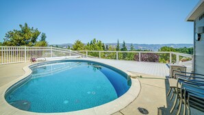 A swimming pool with a view of mountains, a deck with chairs, and a white fence.