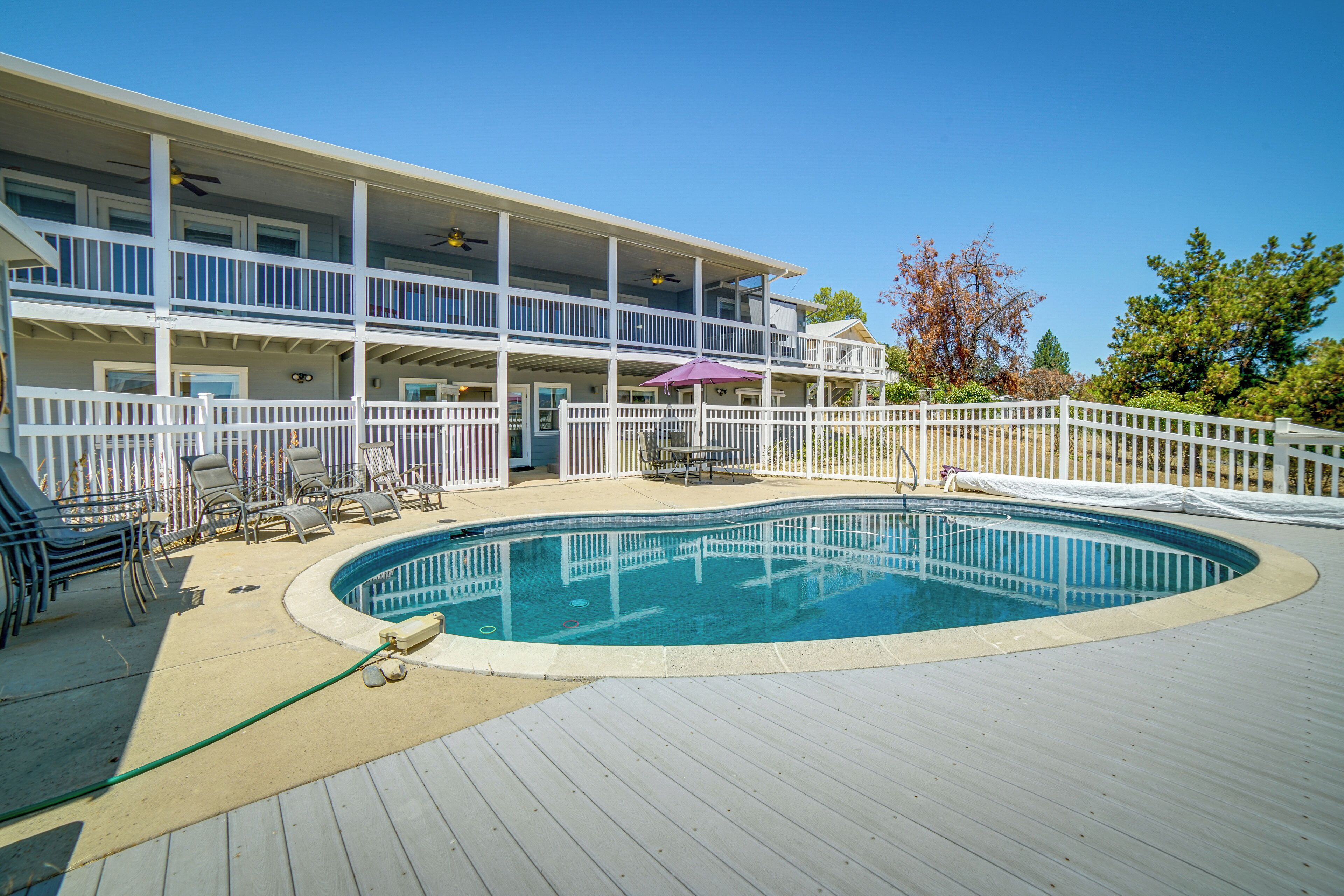 A two-story building with a pool deck, outdoor furniture, and a white fence.
