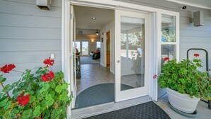 A house entrance with a sliding glass door, a doormat, and potted plants with red flowers.